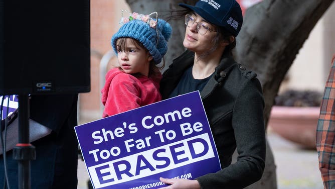 Myra Wood holds daughter, Remi Wood as they show up to support the Independent Women s Forum's \"Our Bodies, Our Sports: We Won't Back Down" rally in Phoenix.