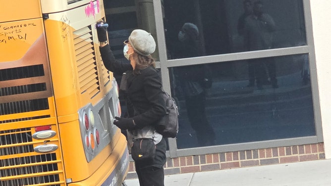 A masked woman writing "protect trans kids" on the Independent Women's tour bus.