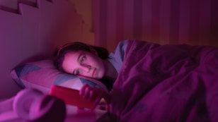 Young girl watching something on her cell phone before going to sleep at night.
