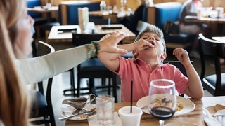 Mother stopping son eating noodles in restaurant