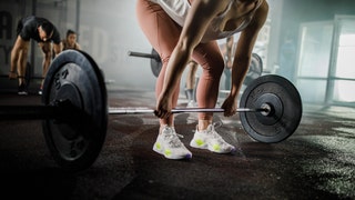 598ea258-Unrecognizable female athlete exercising with barbell in a gym.