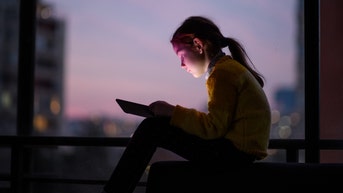 Girl concentrated on playing with stablet at sunset