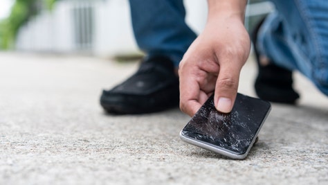 man picking up broken smartphone from the ground