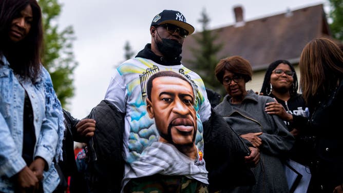 Terrence Floyd removes his jacket to show a shirt bearing the face of his brother, George Floyd, during a vigil in Minneapolis, Minnesota.