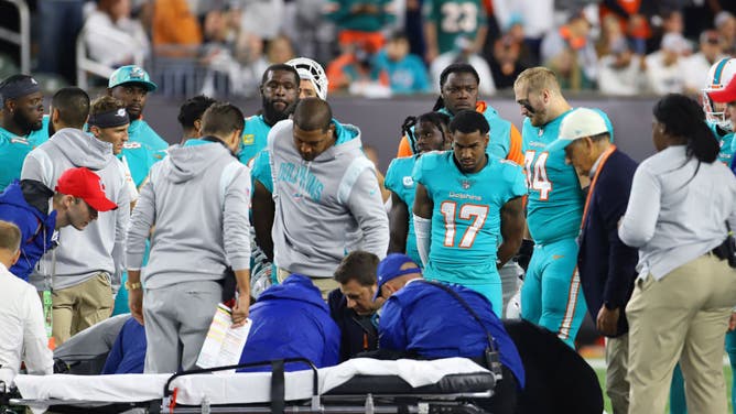 Dolphins players look on as quarterback Tua Tagovailoa is carted off the field as part of NFL Concussion protocol.