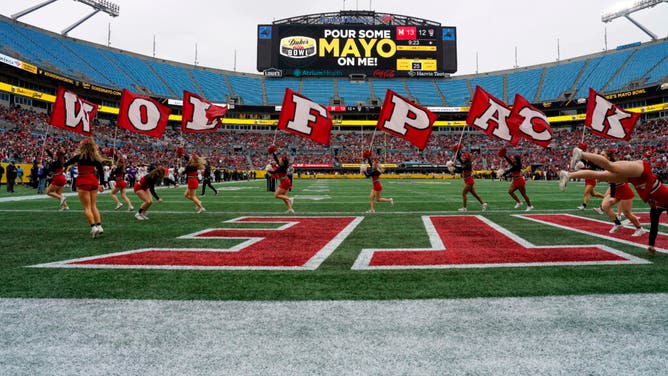NC State Wolfpack cheerleaders run across the end zone with team flags vs. Maryland in the 2022 Duke's Mayo Bowl.