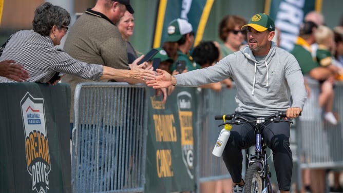 Packers coach Matt LaFleur high-fives a fan as he rides a bicycle to practice at Lambeau Field.