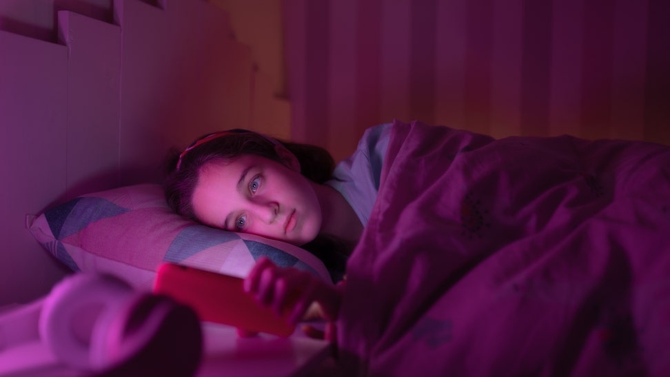 Young girl watching something on her cell phone before going to sleep at night.