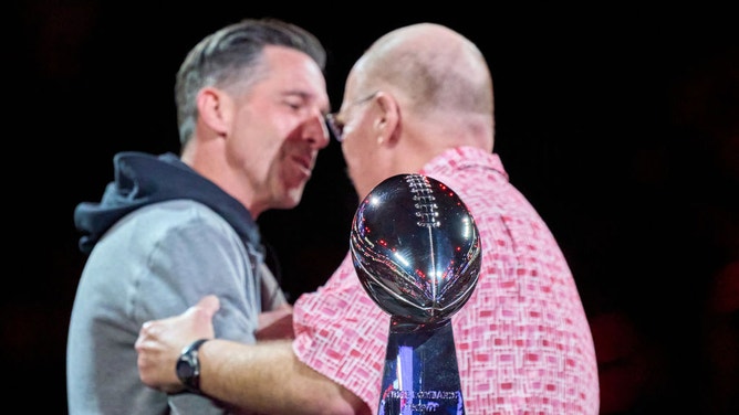 Head Coach Kyle Shanahan of the San Francisco 49ers (L) and Head coach Andy Reid of the Kansas City Chiefs (R) greet each other on stage behind the Vince Lombardi Trophy during Super Bowl LVIII Opening Night at Allegiant Stadium ahead of Super Bowl LVIII on February 5, 2024 in Las Vegas, Nevada.