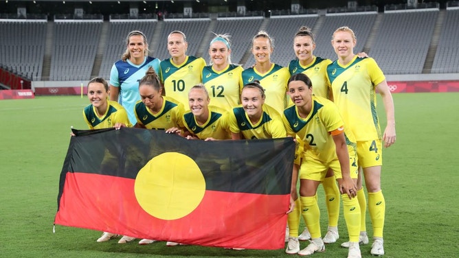 Sam Kerr (#2) and her Matildas teammates pose for a team photo with the Australian Aboriginal flag prior to the Tokyo 2020 Olympic Games match against New Zealand.