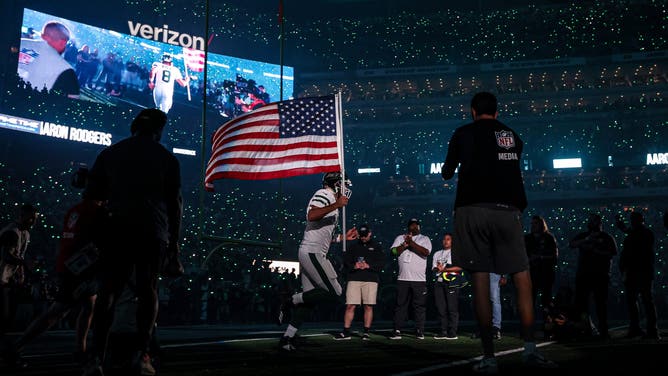 New York Jets quarterback Aaron Rodgers runs onto the field holding the American Flag prior to the team's 2023 season-opening game against the Buffalo Bills. 