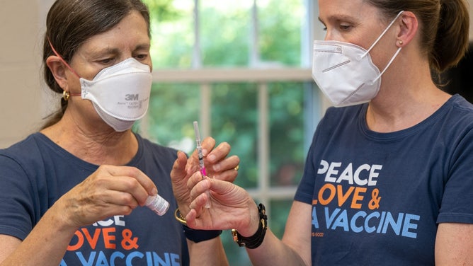 Two women preparing to give COVID vaccines to children