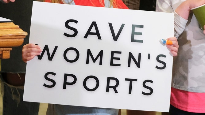 A young girl holds a sign that says, "Save Women's Sports."