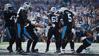 Carolina Panthers running back Rico Dowdle celebrates a touchdown as teammates point toward him on the field in front of the home crowd.