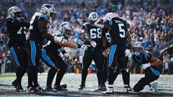 Carolina Panthers running back Rico Dowdle celebrates a touchdown as teammates point toward him on the field in front of the home crowd.