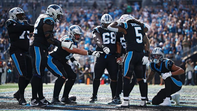 Carolina Panthers running back Rico Dowdle celebrates a touchdown as teammates point toward him on the field in front of the home crowd.
