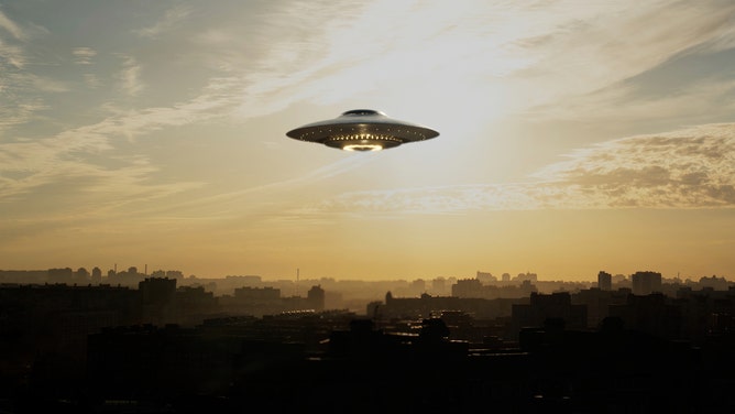 A strange flying machine in the shape of a saucer, silently hovering in the air. It emits a bright light and seems to scan the surrounding space with a beam. (Credit: Getty Images Creatives)