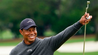 tiger woods smiling, holding his putter