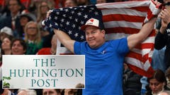 A USA fan holds an American flag during the Olympics and a Huffington Post logo is in the lower left corner of the photo.