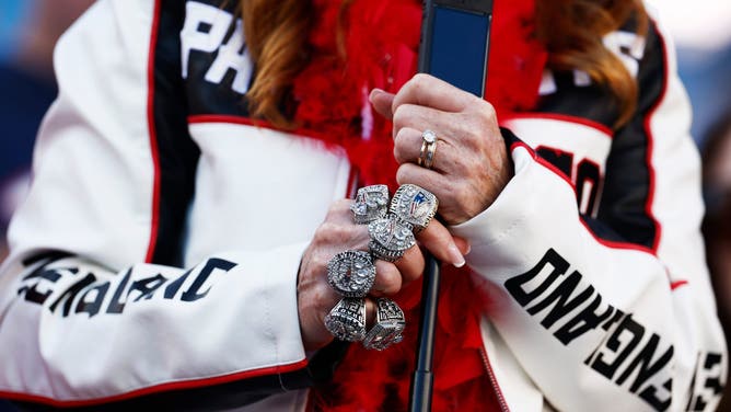 A New England Patriots fan wearing replica Super Bowl rings watches the team warm up before Super Bowl LX.